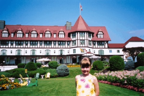 young girl in yellow and pink flowered top standing in front of the Algonquin Resort in St. Andrews-by-the-Sea, New Brunswick with flower gardens.