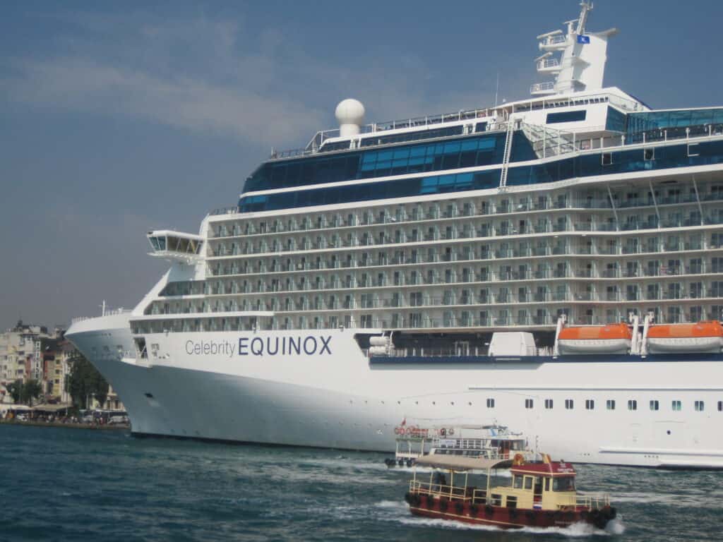 Front half of Celebrity Equinox in port with two small passenger boats alongside.