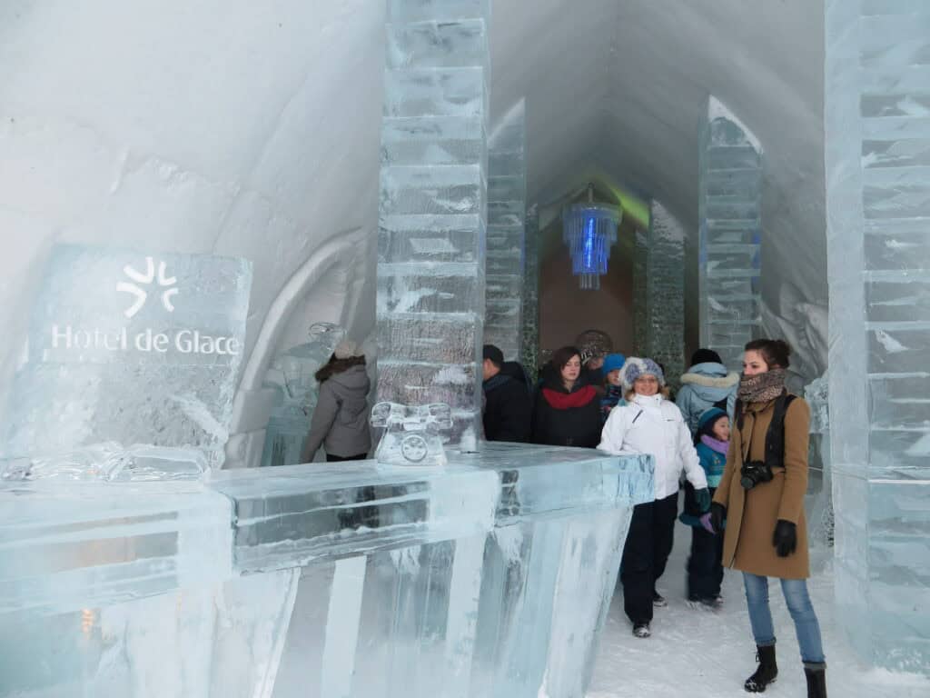 people standing near reception desk and entrance to great hall at quebec ice hotel.