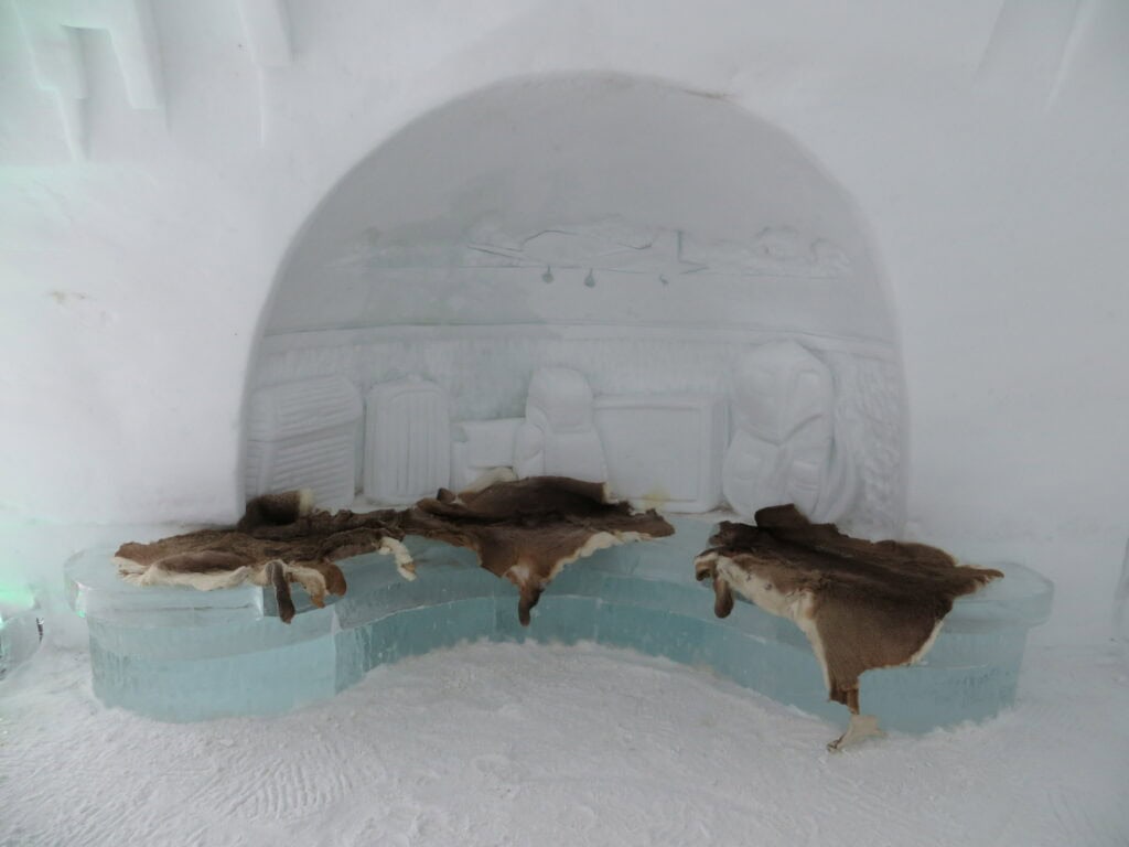 ice bench with three brown furs to sit on - quebec ice hotel