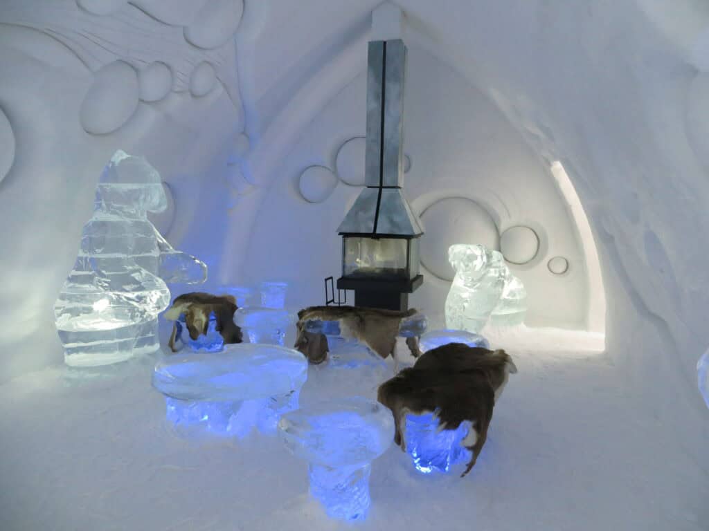 quebec ice hotel - seating area in a premium suite with ice chairs, furs and small fireplace/stove.
