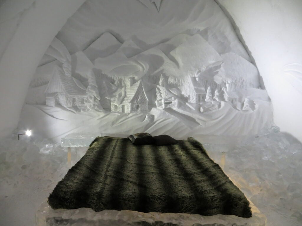 Legends of Quebec room at Ice Hotel with Quebec village mural carved in headboard.