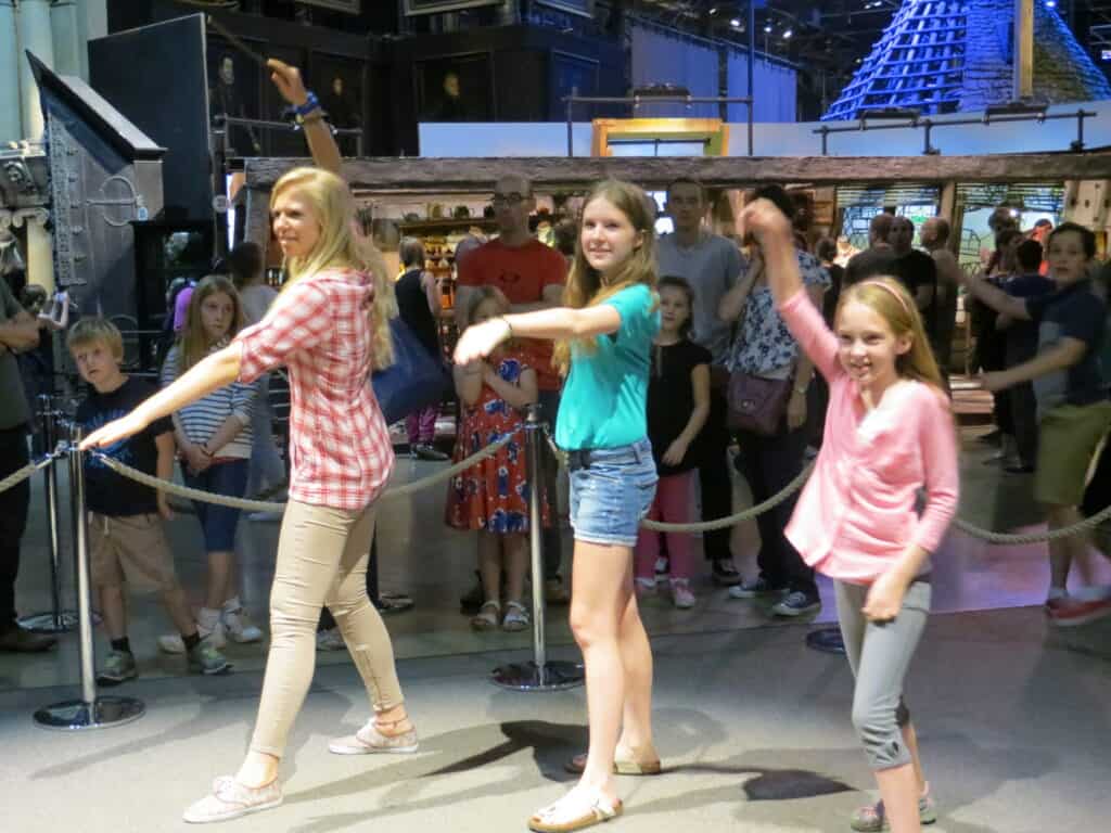two teen girls and one younger girl pretending to hold wands casting spells at the making of harry potter.