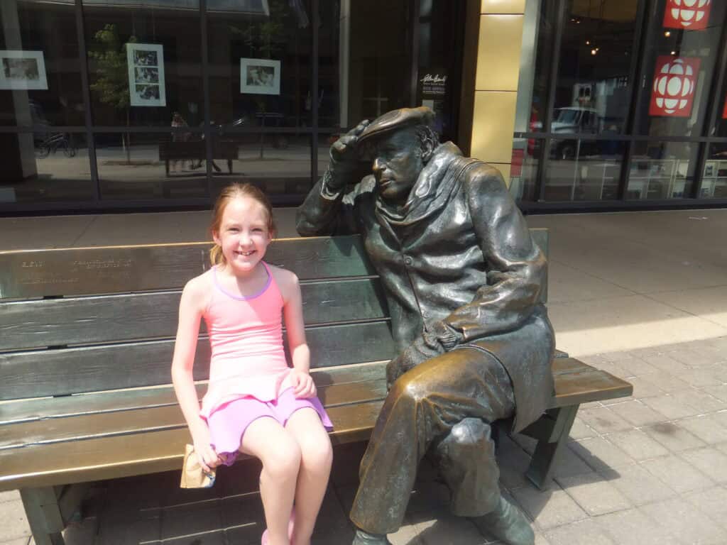 young girl dressed in pink sitting on Glenn Gould bench in Toronto.