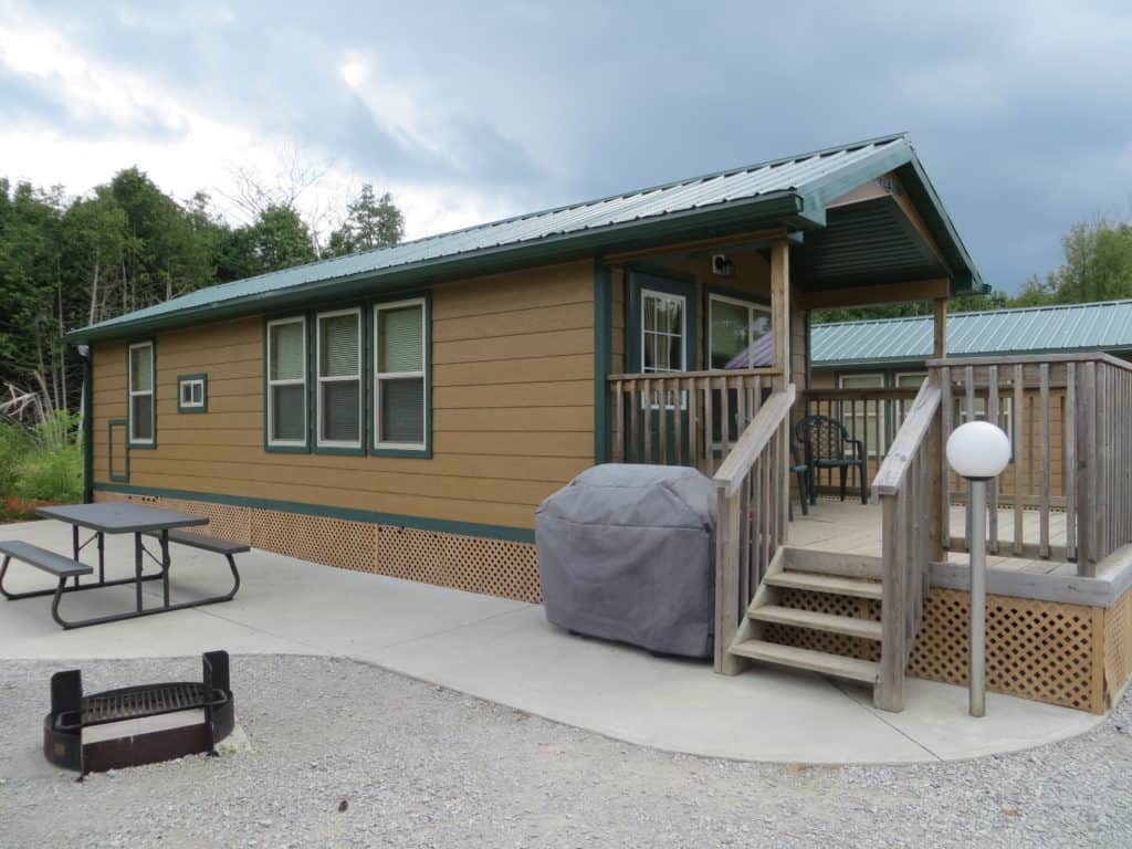 cabin with brown siding and green trim, deck and paved patio with picnic table and covered barbecue.