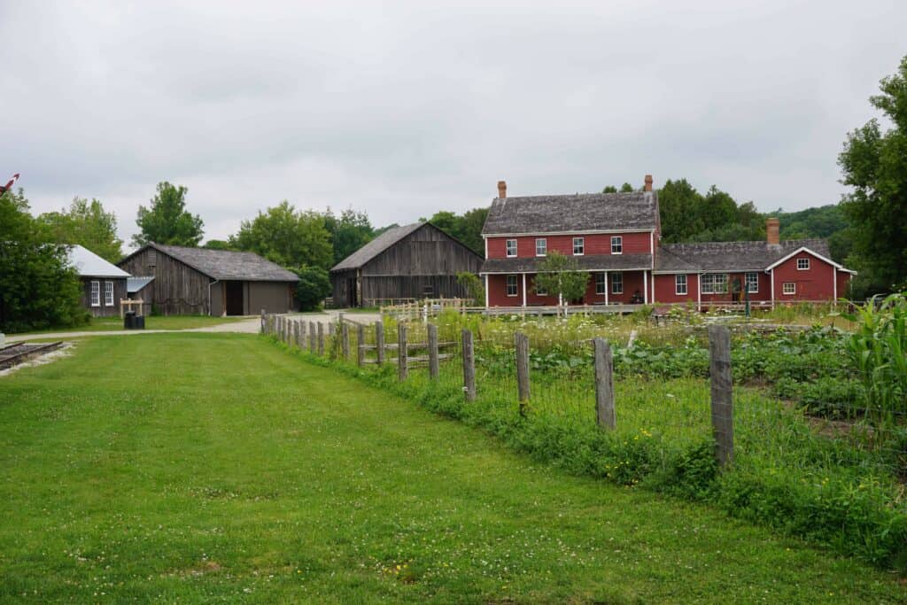 field in front of heritage buildings - red siding on house and grey outbuildings.