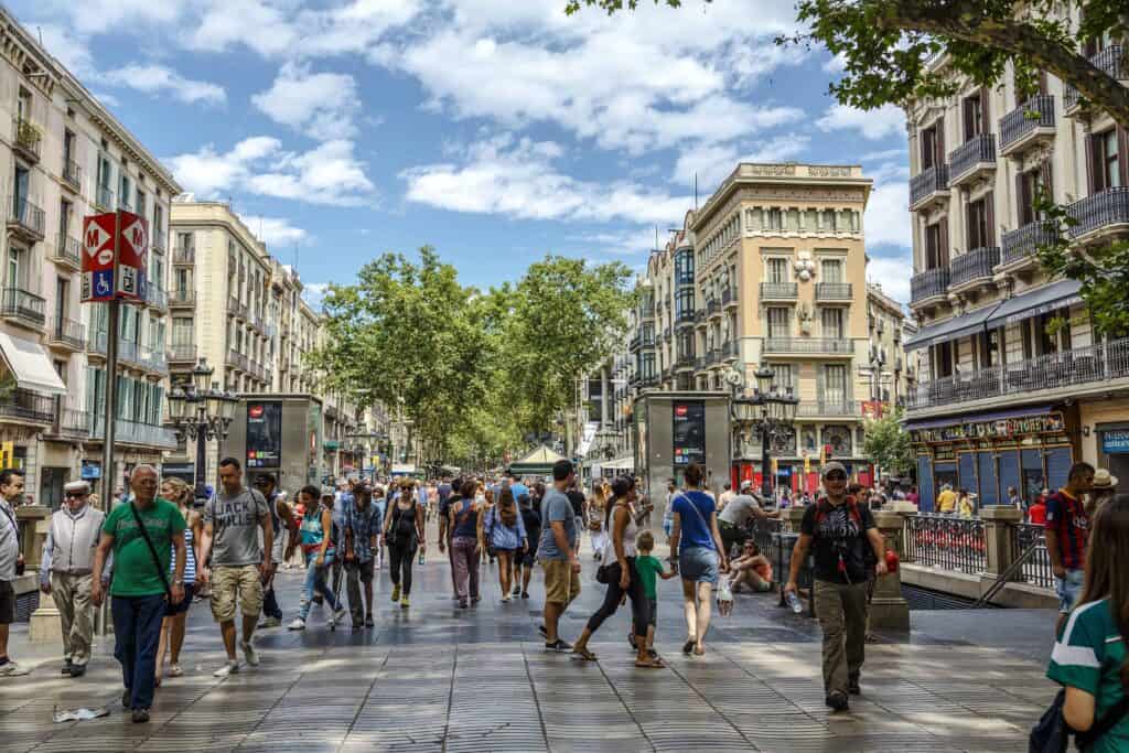 People walking on La Rambla in Barcelona on a summer day with blue sky and a few white clouds.