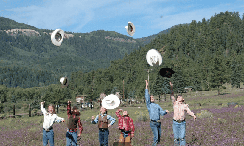 group of kids throwing cowboy hats in air with mountains in background.