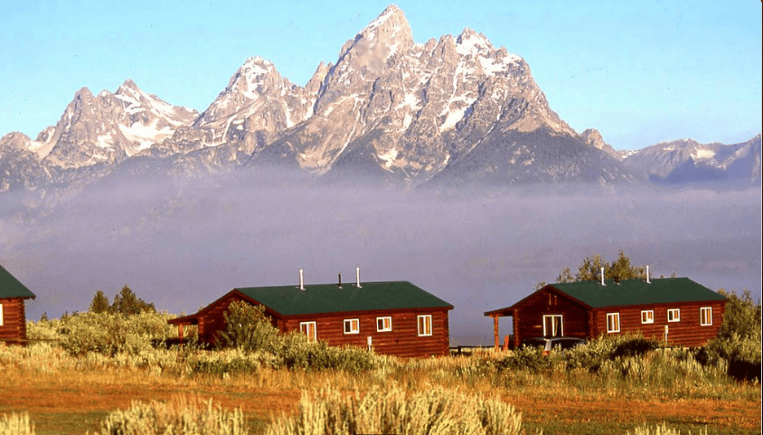 Triangle X Ranch in Jackson Hole - two reddish brown buildings with four windows, dark roofs and mountains in background.