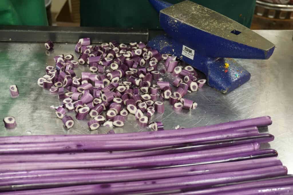 strips of purple hard victorian candy and pile of cut pieces purple and white inside on metal counter.