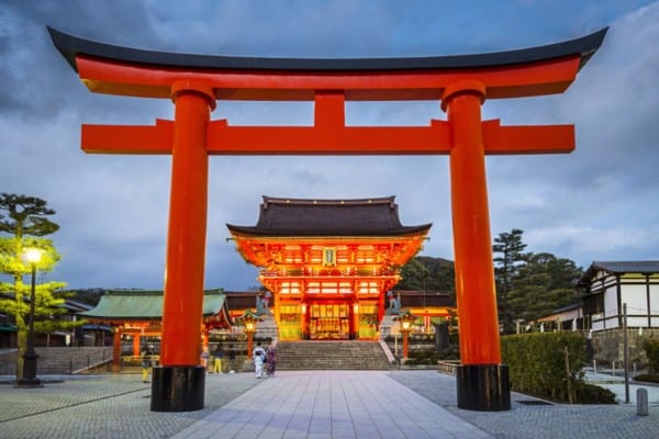 large red archway with temple behind - Fushimi Inari Shrine in Kyoto, Japan.
