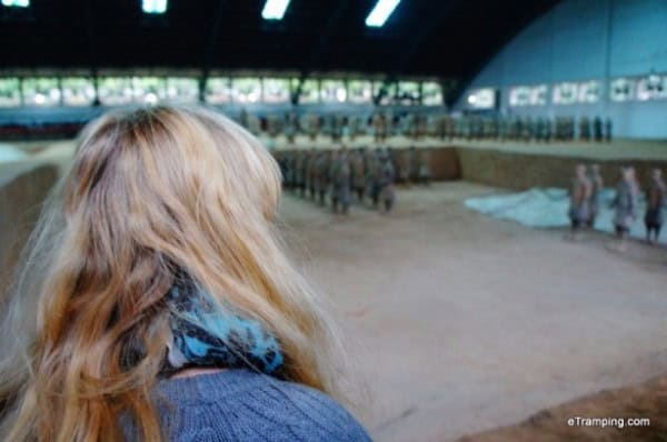 blond woman in blue top viewed from behind as she admires the terracotta warriors, china.