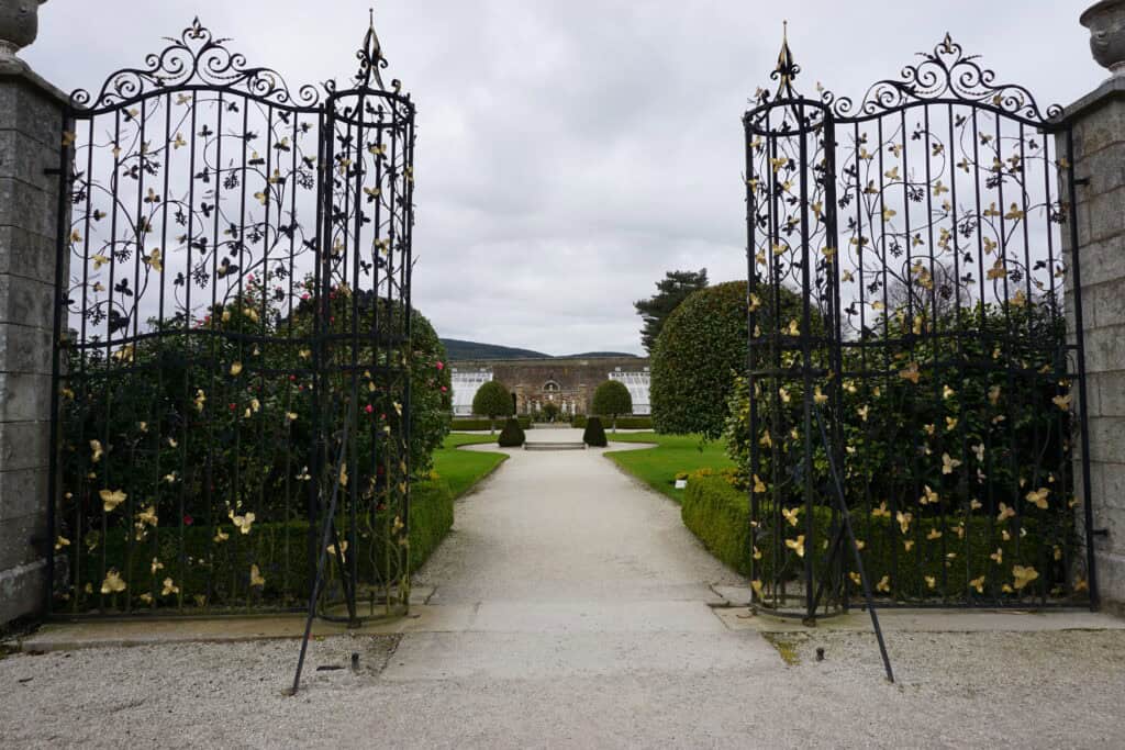 Elaborate wrought iron Venetian Gate with bushes and garden in background.