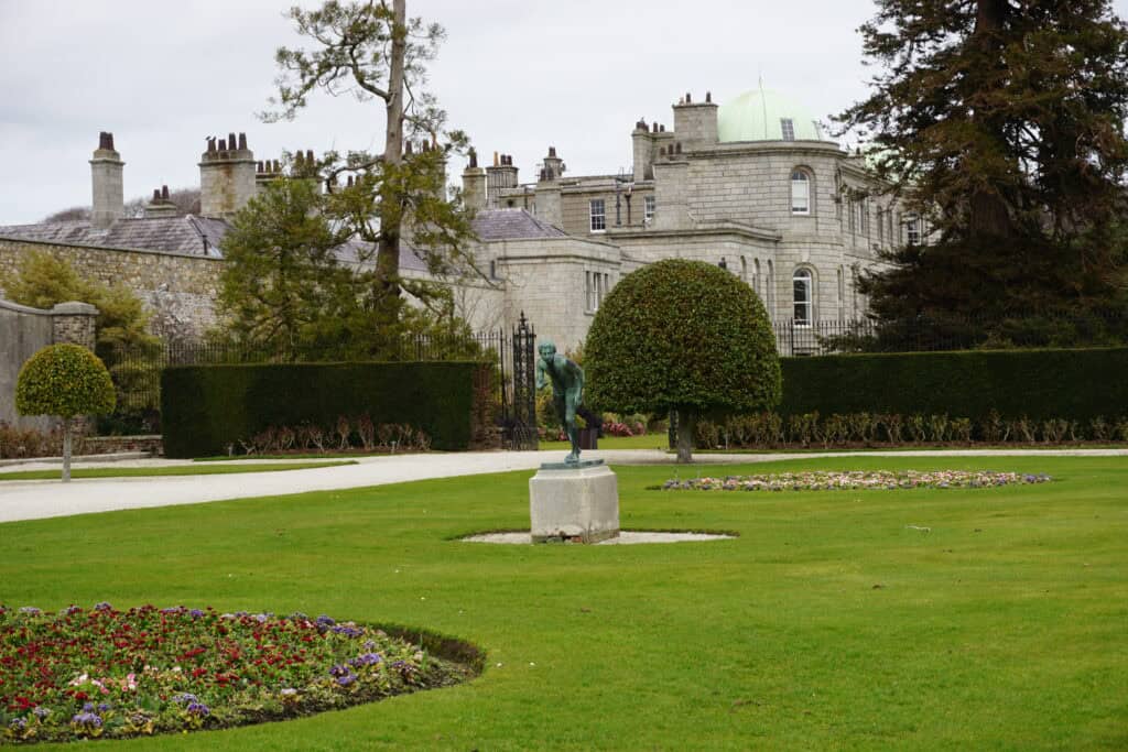 statue on green lawn and flower bed in foreground of Powerscourt House.