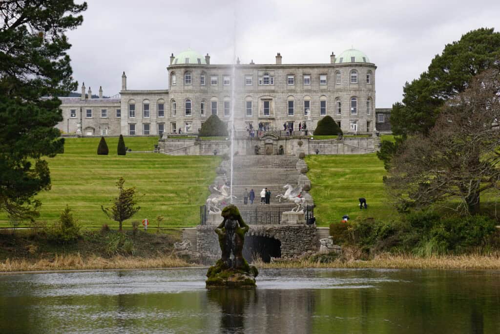 Fountain in body of water with stone steps and Powerscourt House in background.