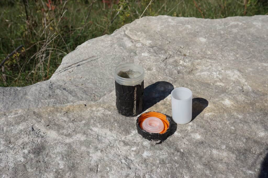 small black film canister, lid and white canister sitting on large rock.