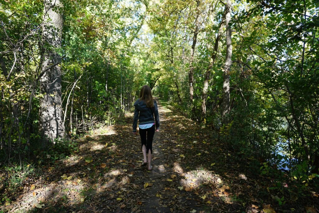 young girl walking on trail through wooded area viewed from behind.