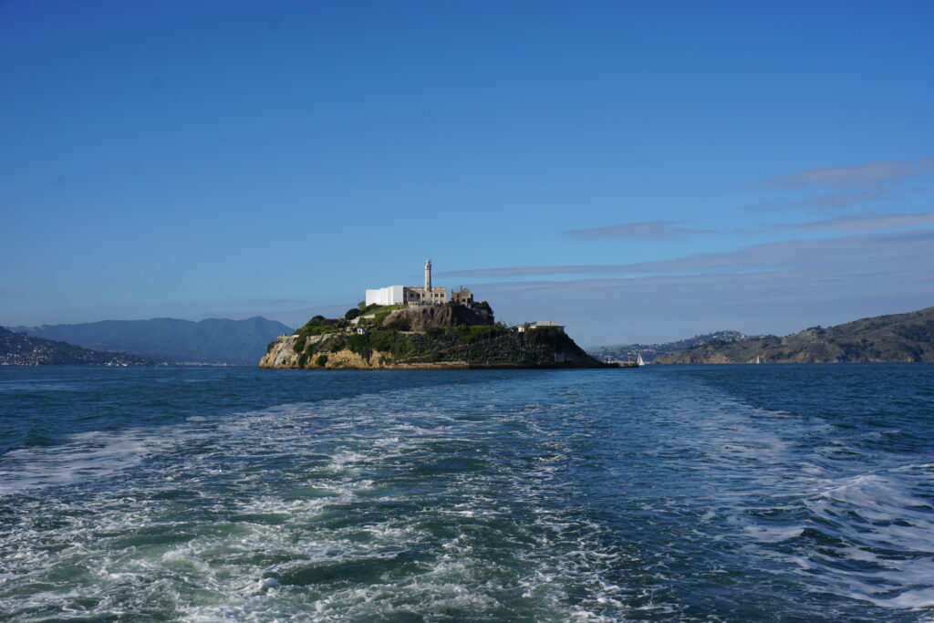 View of Alcatraz Island across the water approaching by ferry set against a bright blue sky.