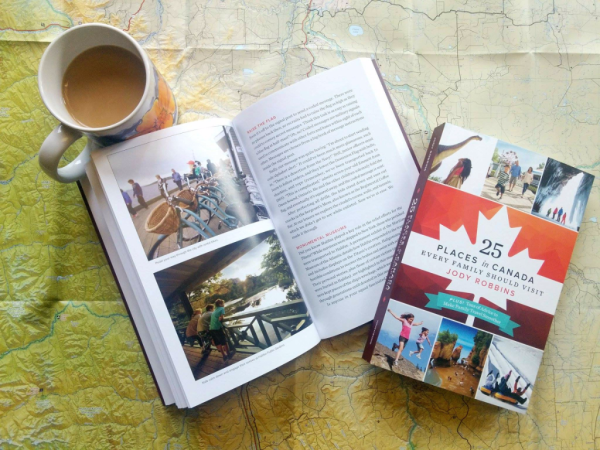 An open copy and a closed copy of book 25 places in canada every family should visit sitting with a cup of coffee on top of a map.