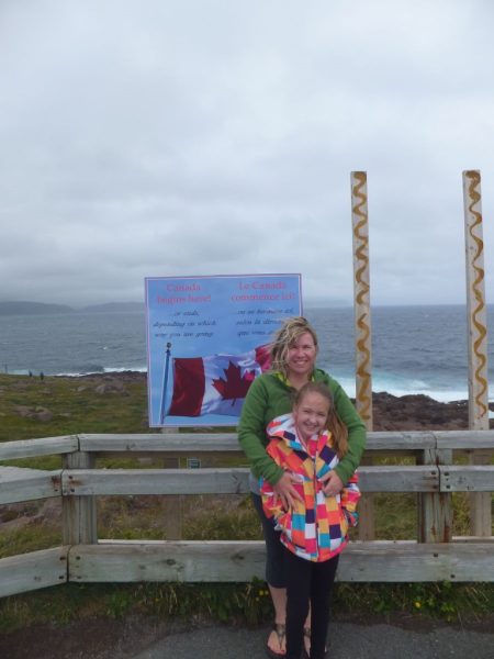 Woman in green sweater and young girl in colourful coat at Cape Spear, Newfoundland sign.