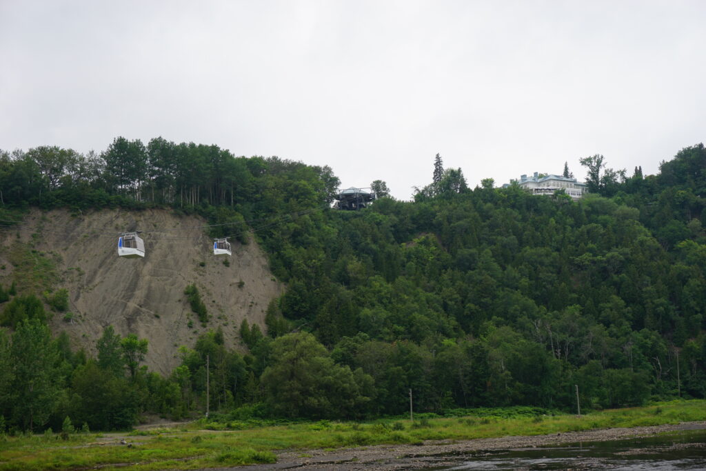 two white cable cars visible against treed cliff with Manoir Montmorency at top.