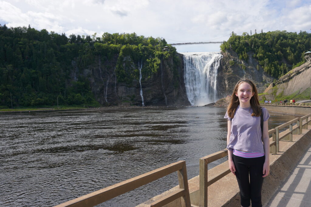 young teen girl in black pants and purple t-shirt posing on boardwalk with Montmorency Falls in background - Quebec City.