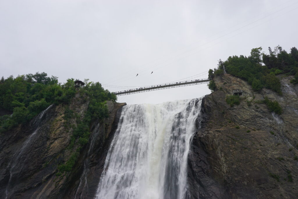Two very small appearing people above the suspension bridge ziplining across Montmorency Falls, Quebec.