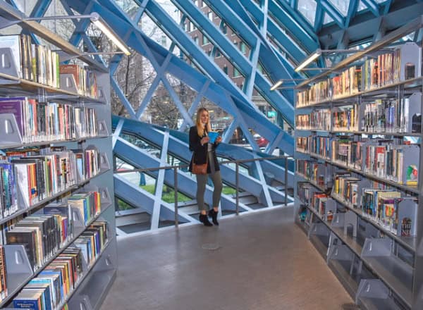 Woman standing in stacks of Seattle Public Library with bright blue beams in background.