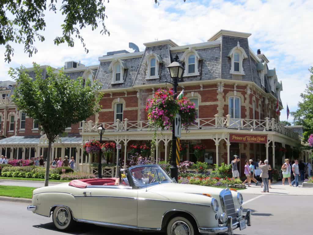 Cream coloured classic convertible in front of Prince of Wales Hotel in Niagara-on-the-Lake on summer day with flowers everywhere.