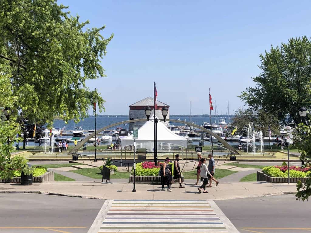people walking in confederation park on the kingston, ontario waterfront with martello tower and boats in the background