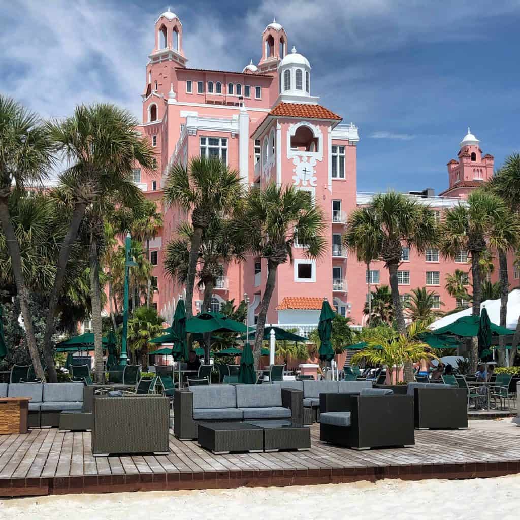 Seating area with wicker chairs on beach with pink hotel in background