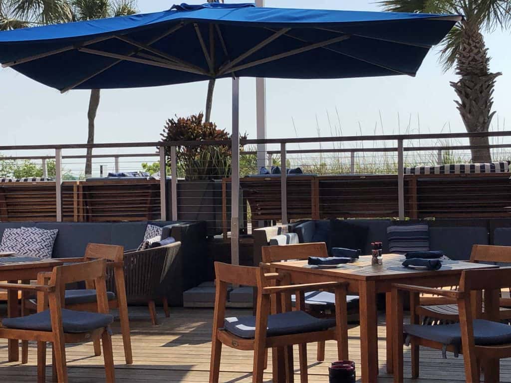 outdoor restaurant with wooden tables and chairs and blue patio umbrella