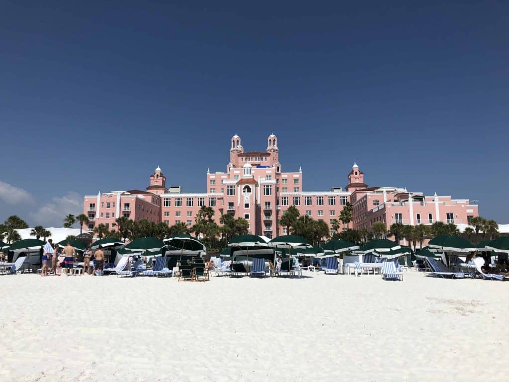green umbrellas and beach chairs on white sand beach with pink hotel in background at the Don CeSar on St. Pete Beach, Florida.