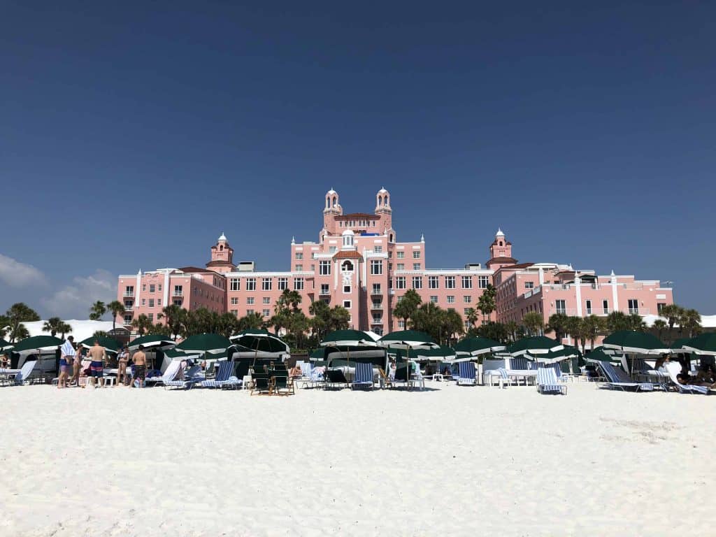 green umbrellas and beach chairs on white sand beach with pink hotel in background