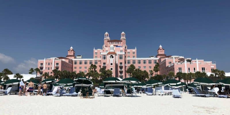 green umbrellas and beach chairs on white sand beach with pink hotel in background