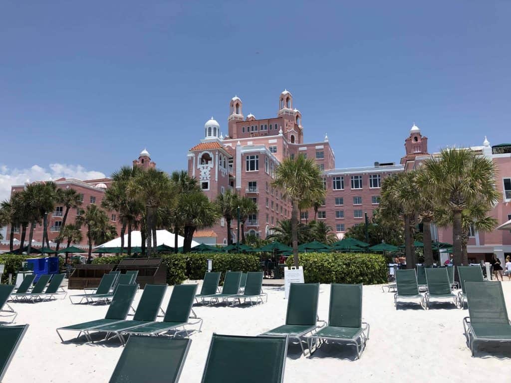 green beach chairs on white sand with pink hotel in background