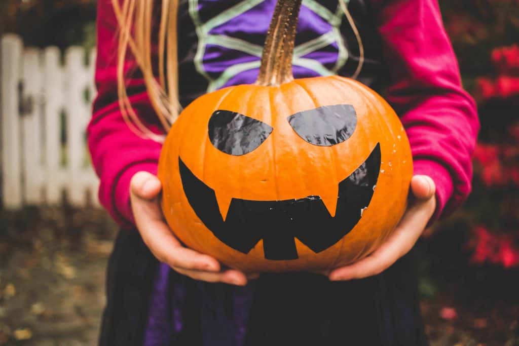 girl in costume holding a painted jack o'lantern