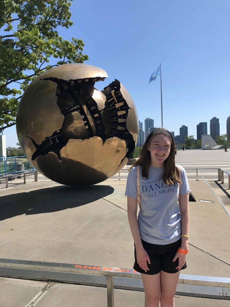 teen in front of round sculpture with UN flag in background