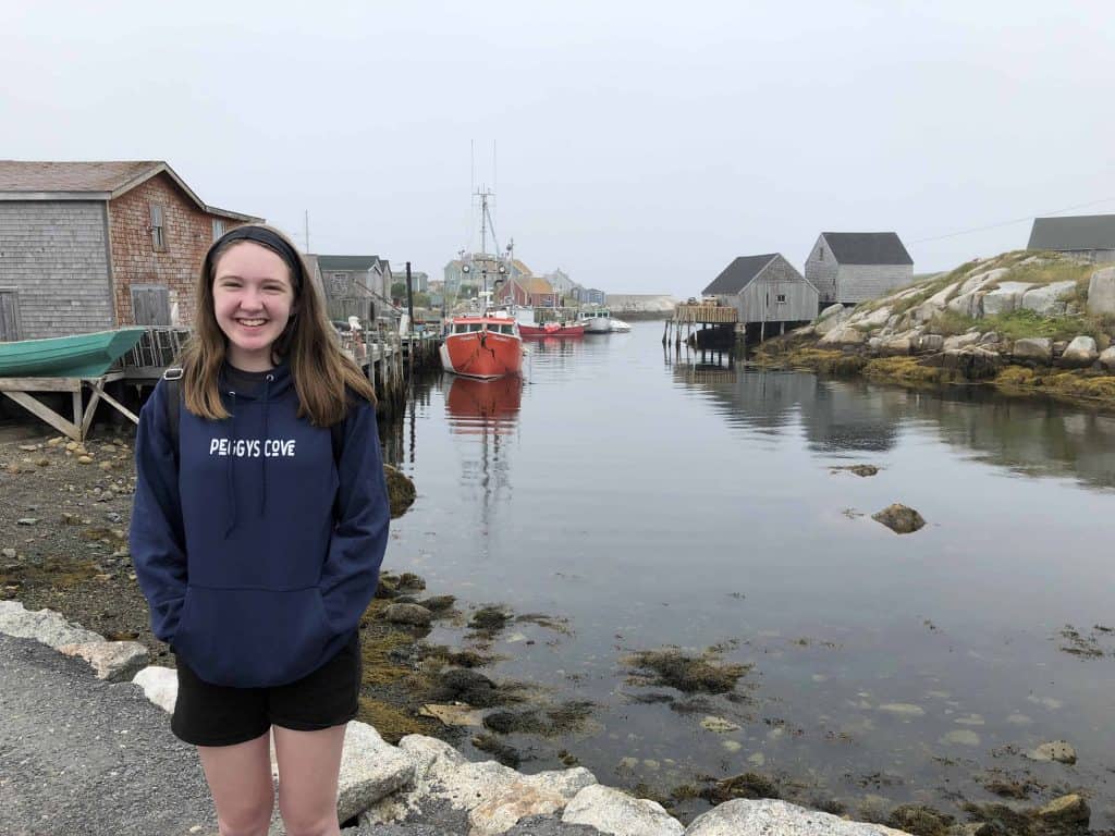 peggy's cove nova scotia-teen girl standing by water with boats and weathered buildings