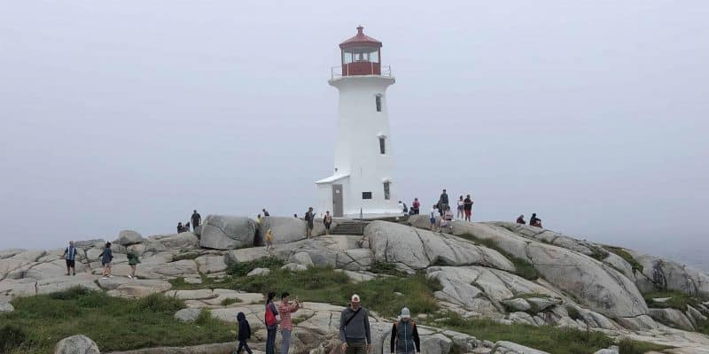 red and white lighthouse on rocks with people around