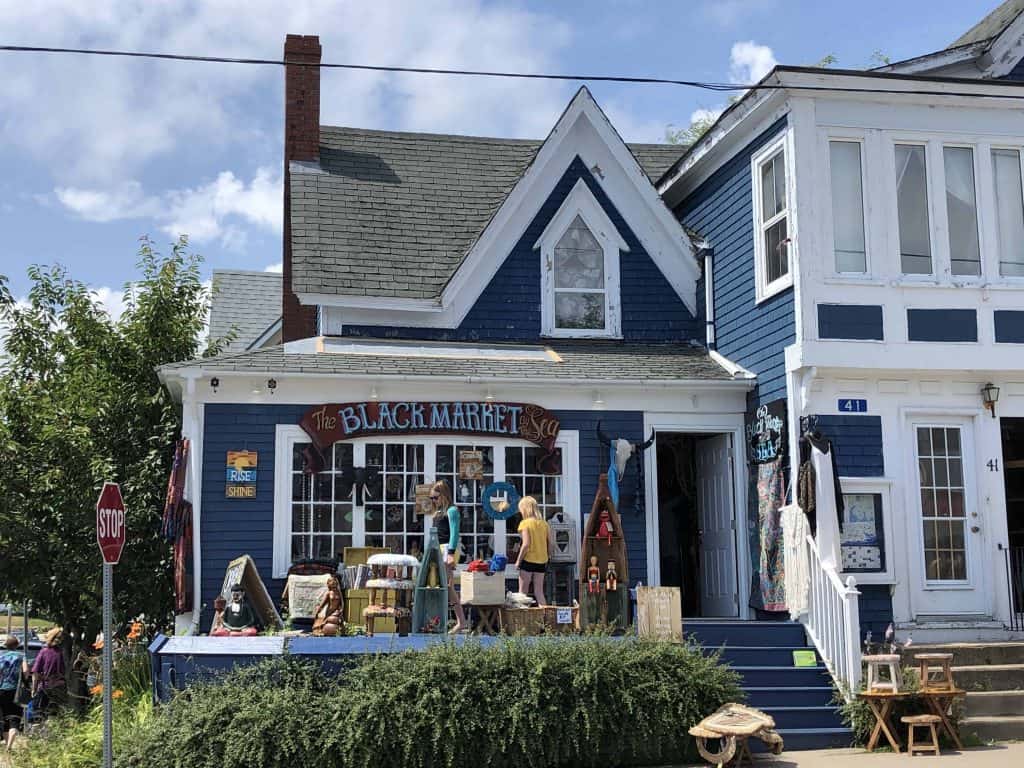 blue clapboard store called The Black Market by the Sea with girls browsing merchandise out front