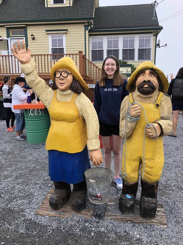 teen girls with wooden figurines of male and female fishermen in front of yellow building