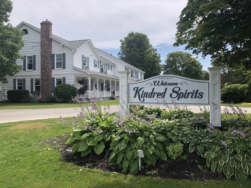 Sign reading "Welcome Kindred Spirits" with inn in background at kindred spirits country inn in Cavendish, PEI.