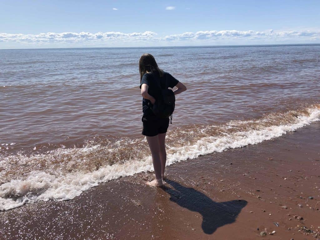 teen girl standing on beach looking at ocean