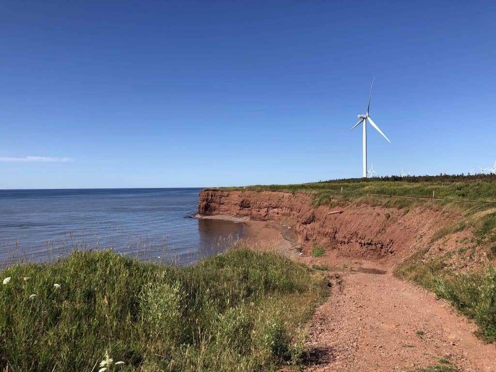 windmills along coast line with red sand cliffs - prince edward island north cape coastal drive