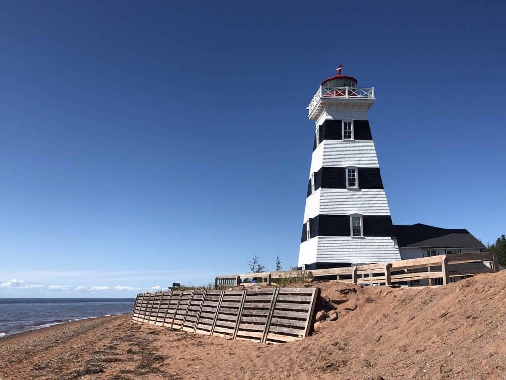 Black and white striped lighthouse on beach by ocean