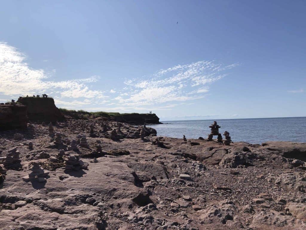 inukshuks on rocky shore by ocean - north cape prince edward island