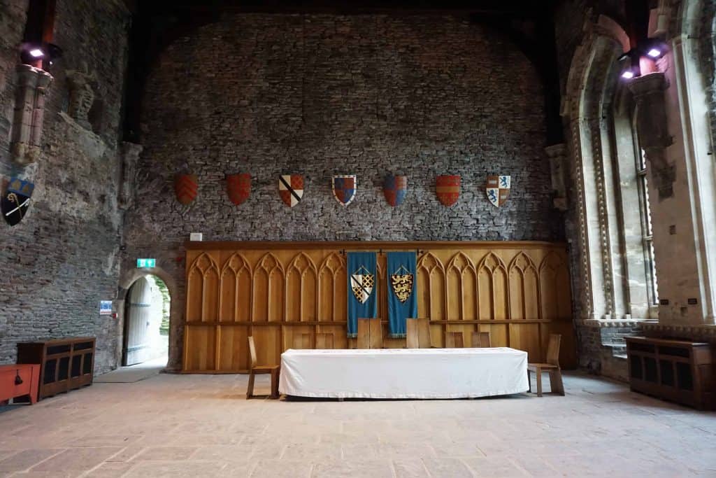 room inside of ancient stone castle with table and chairs and wall decorated with crests