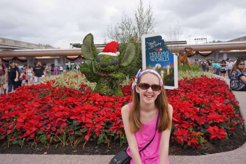 girl in front of poinsettias and Stitch topiary with santa hat