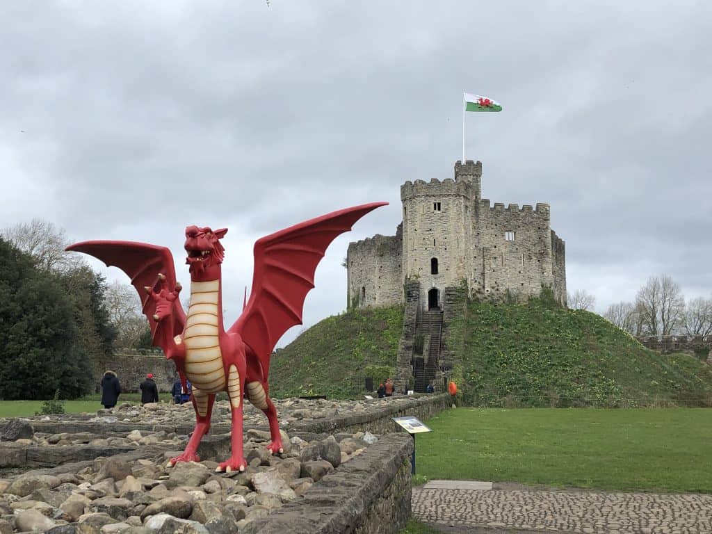 red dragon in front of stone castle on hill flying welsh flag